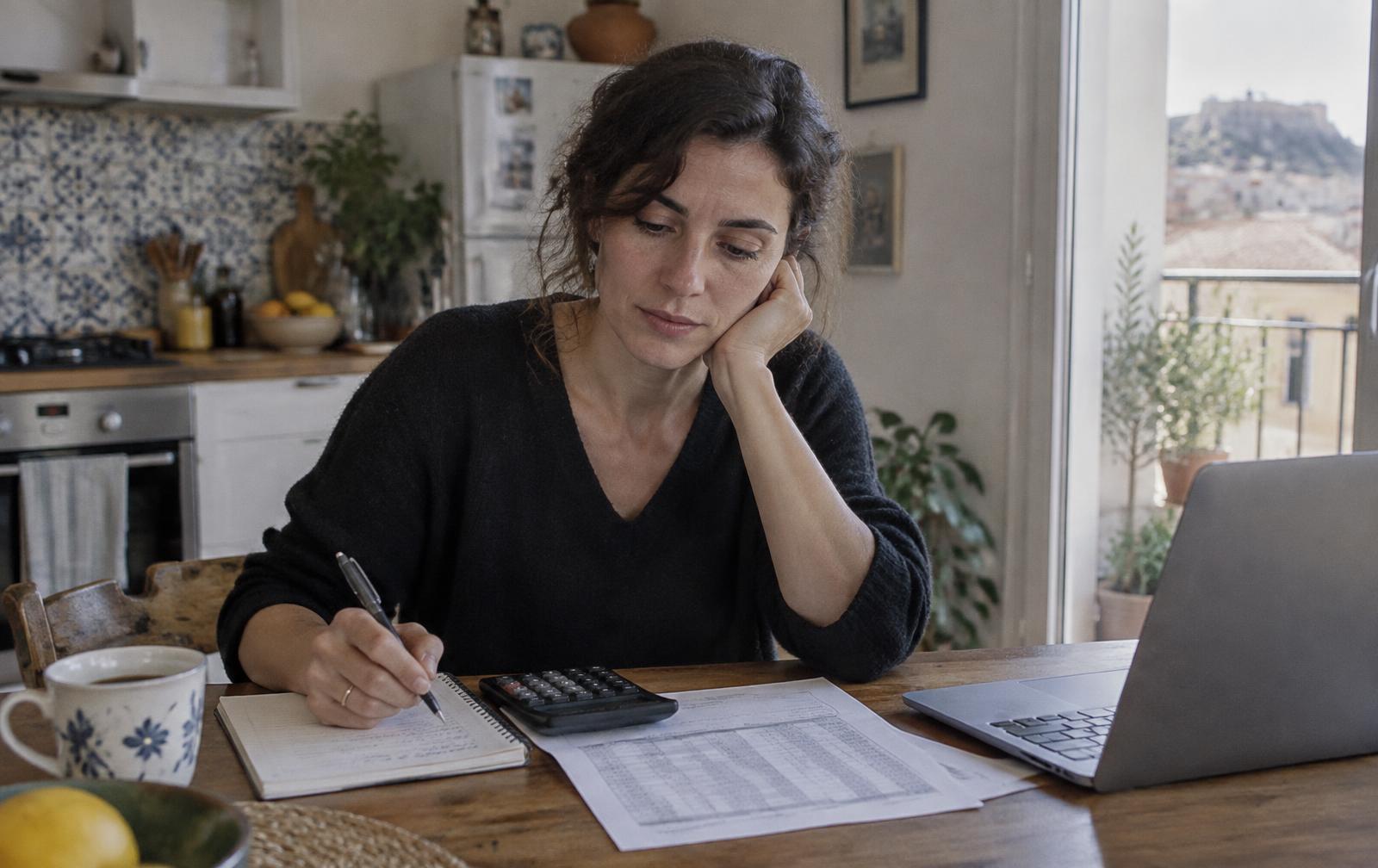 Femme calculant la mensualité de son prêt immobilier à sa table de cuisine, carnet et calculatrice