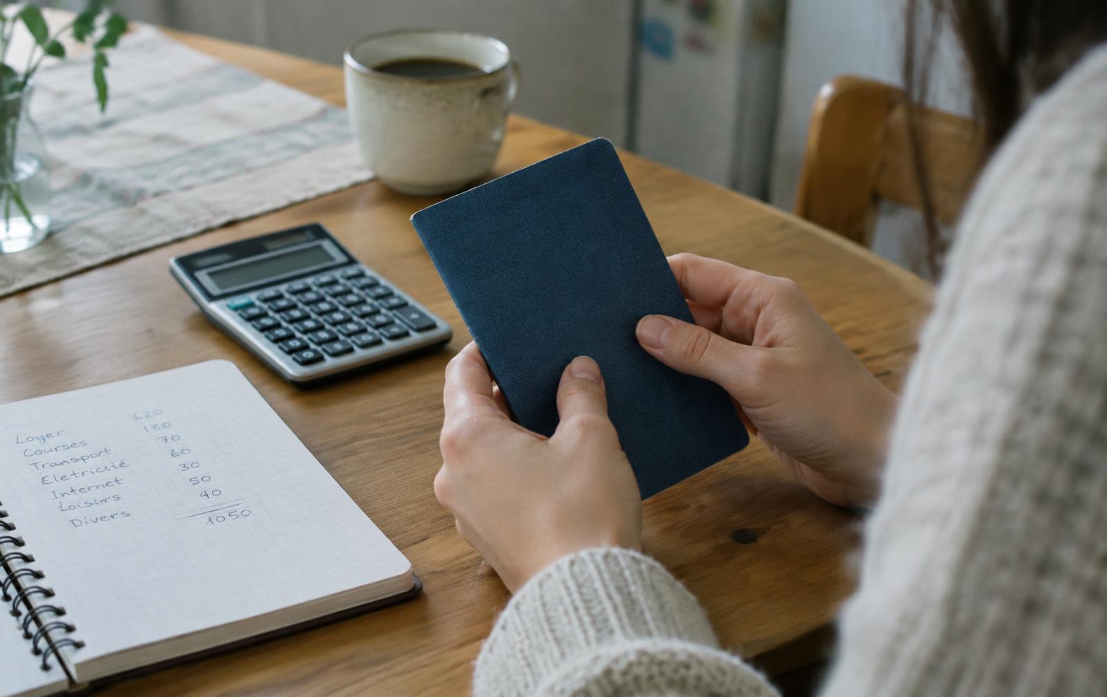 Mains d'une jeune femme tenant un livret d'épargne à côté d'une calculatrice et d'un budget manuscrit
